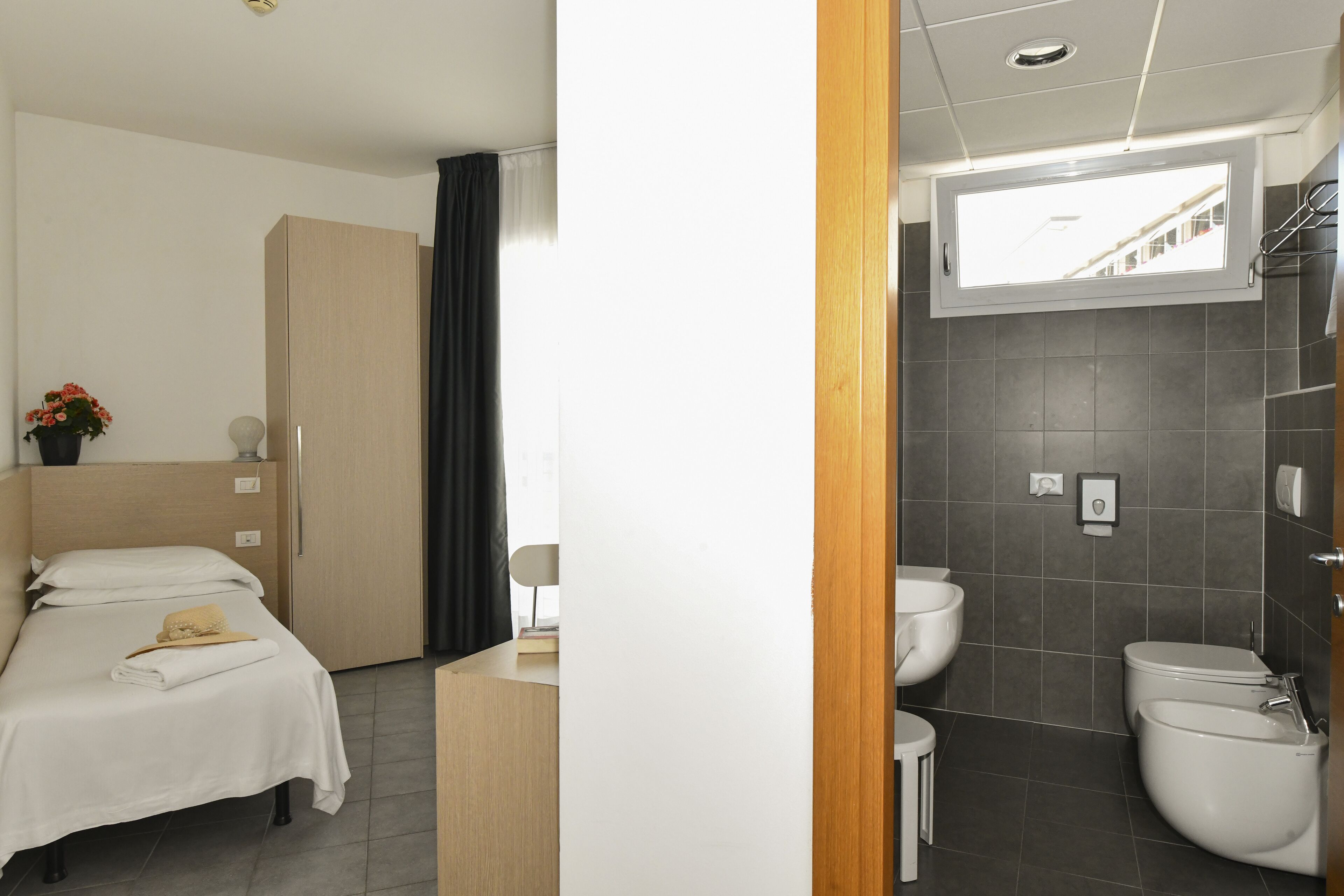 A hotel room with a bed, a desk, a window, a bathroom with a sink, toilet, and bidet.