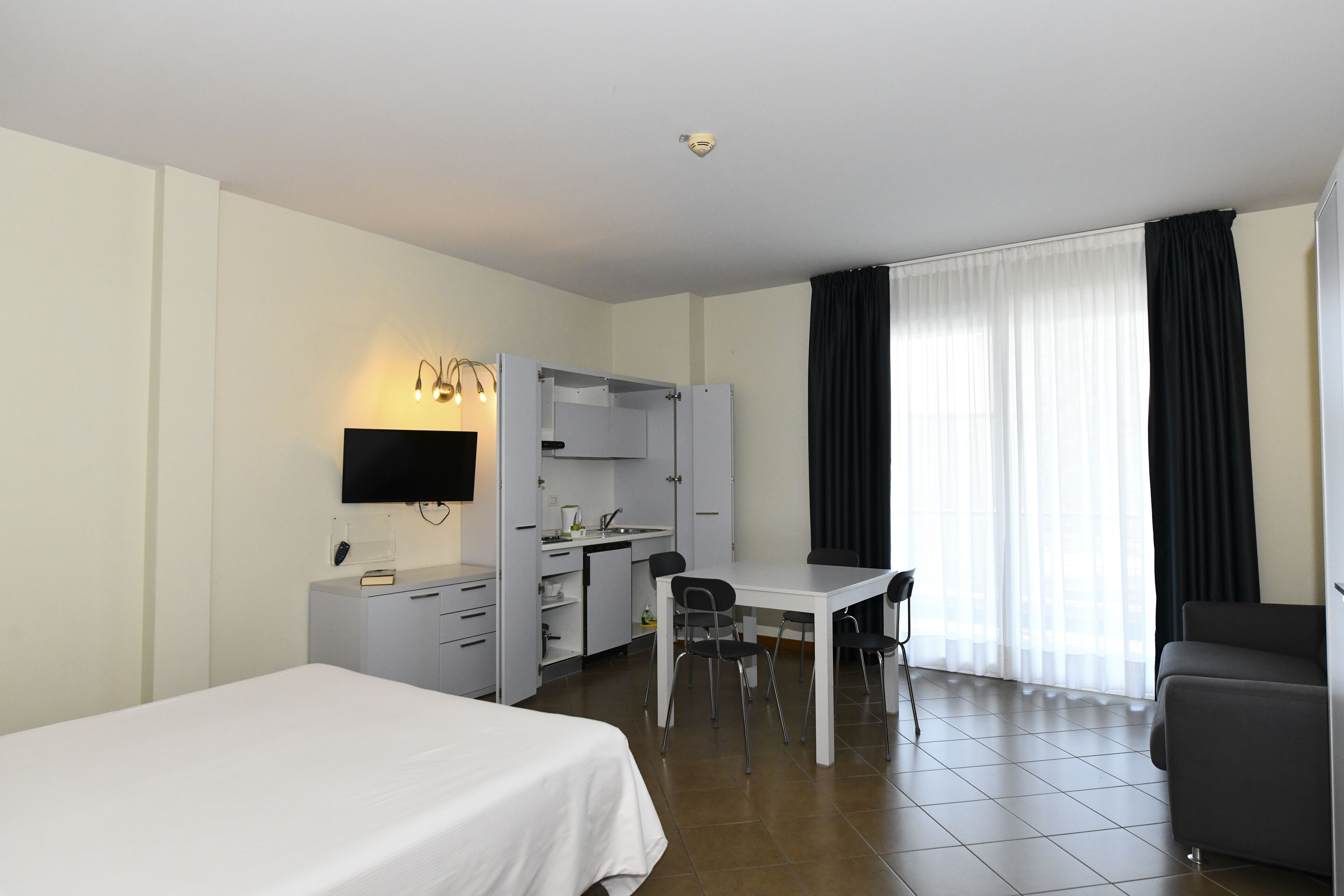 Une chambre d’hôtel équipée d’un lit, d’un bureau, d’une chaise, d’une kitchenette et d’un téléviseur.