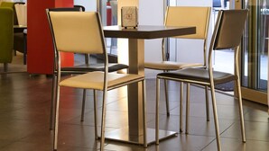 A modern indoor seating area with a table and chairs, large windows, and a potted plant. - Hotel Eden (Jesolo)