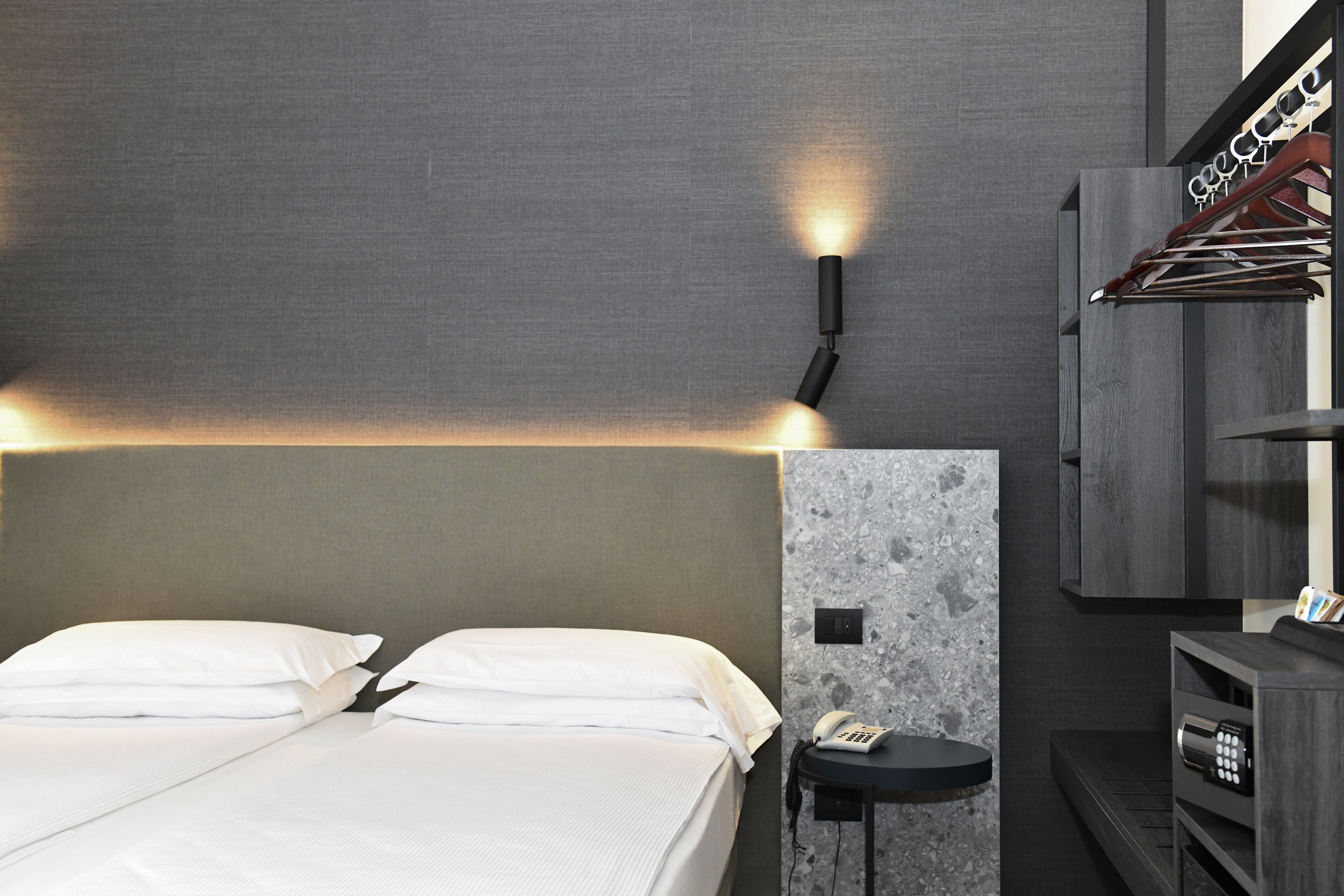 Una camera d'albergo con un letto, un telefono a muro e un comodino con una lampada.