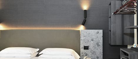 A hotel room with a bed, a wall-mounted phone, and a small table with a lamp.