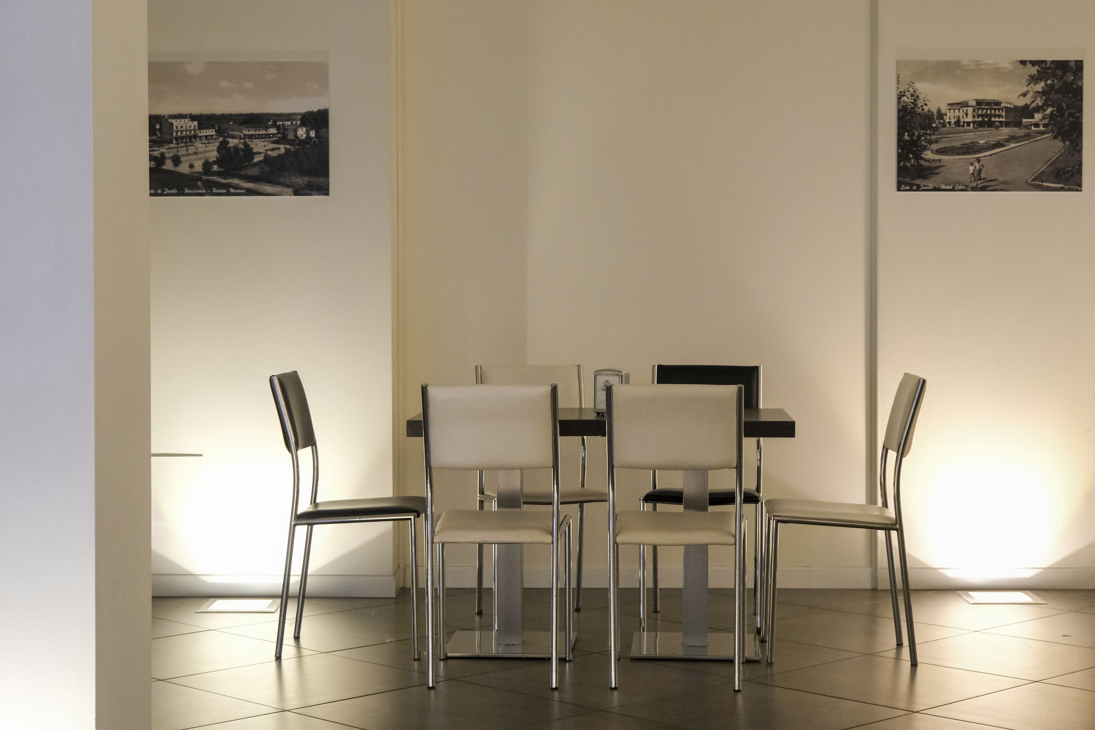 A dining area with four chairs and a table, two black-and-white photographs on the walls, and a tiled floor.