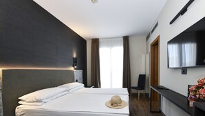 A hotel room with a large bed, a TV, a desk, and a chair. - Hotel Eden (Jesolo)