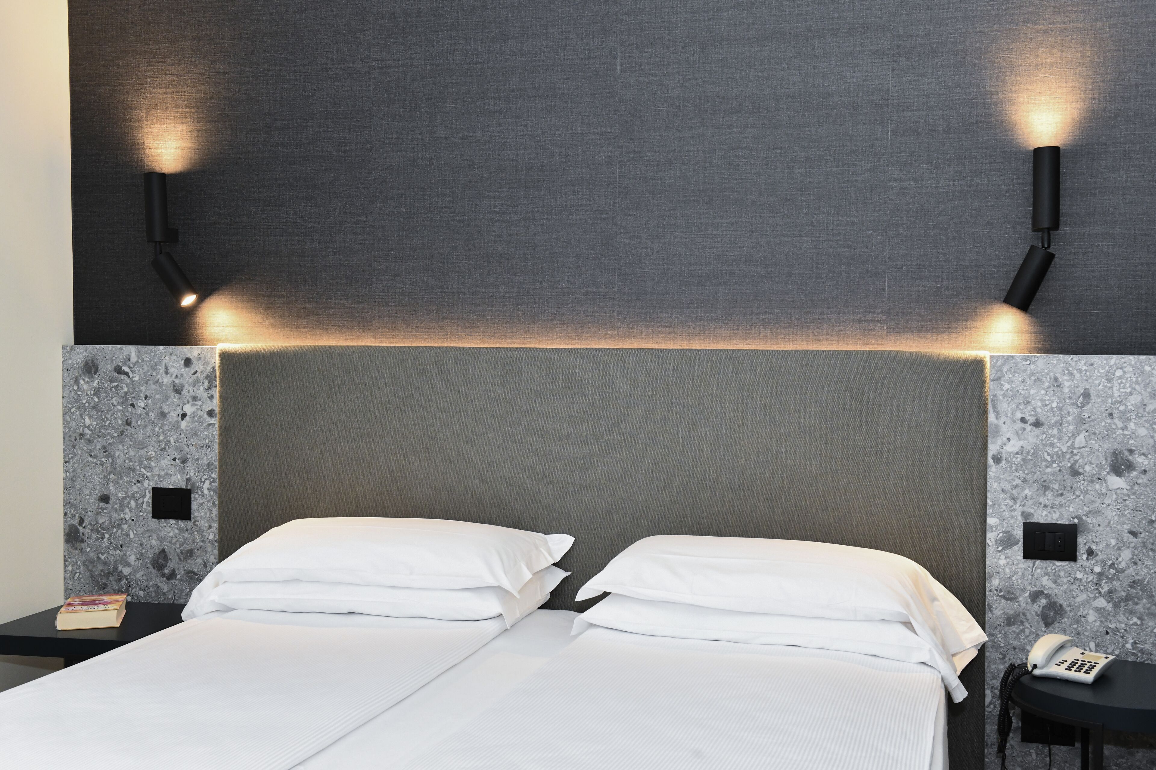 A double bed with white linens, a grey headboard, and two bedside tables with lamps.