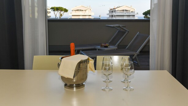 A balcony with two lounge chairs and a table with a metal bowl and three wine glasses. - Hotel Eden (Jesolo)