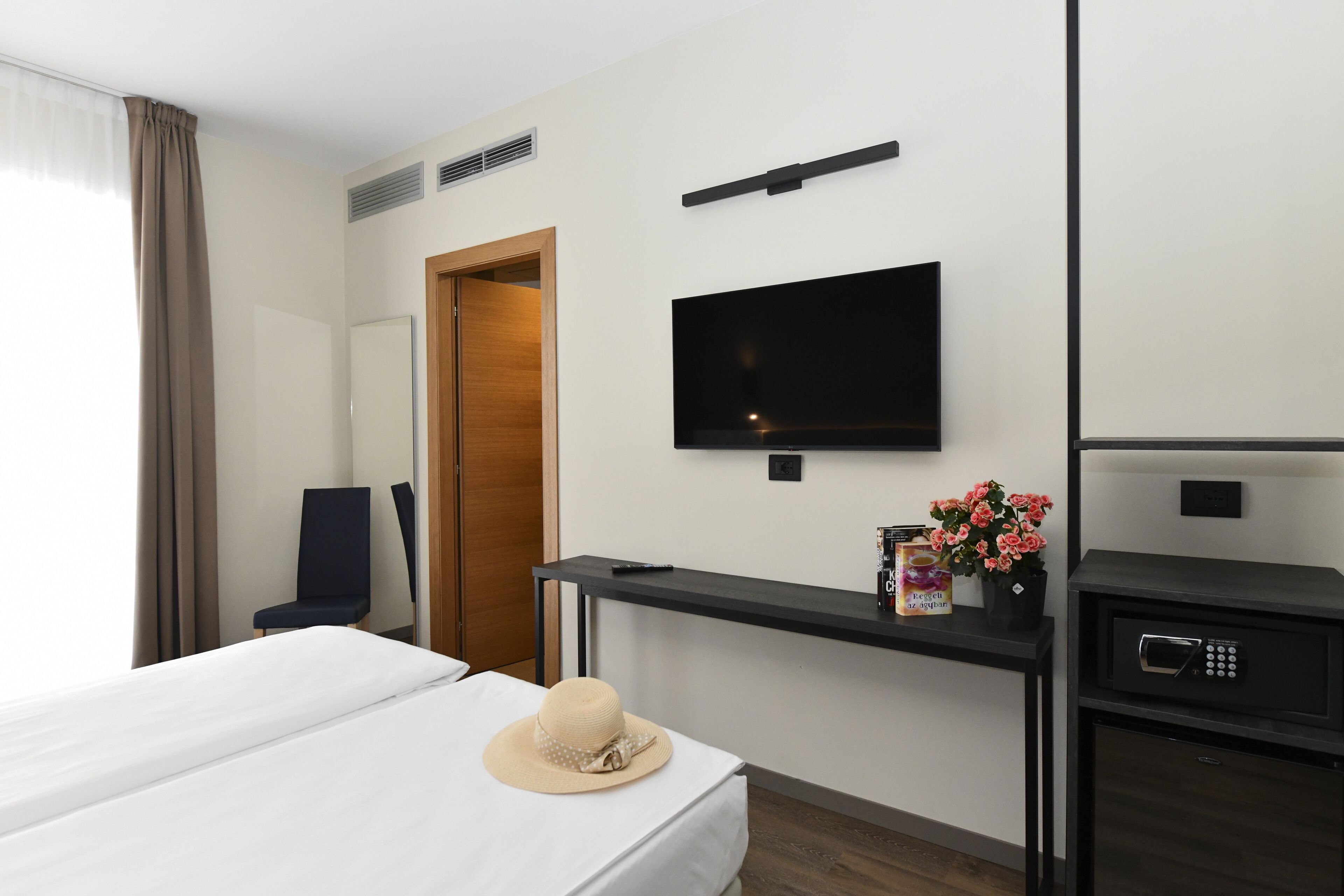 Ein Hotelzimmer mit Bett, Schreibtisch mit Flachbildfernseher, Stuhl, Kleiderschrank und einem kleinen Tisch mit Fernbedienung und Pralinenschachtel.