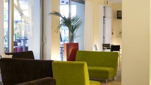 A modern living room with a large window, a potted plant, and two green armchairs. - Hotel Eden (Jesolo)