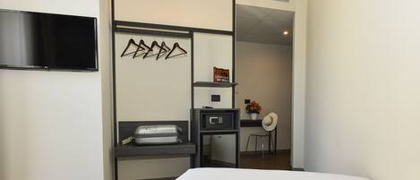 A hotel room with a bed, a flat-screen TV mounted on the wall, a small kitchenette area with a microwave, and a seating area with a chair and a small table.