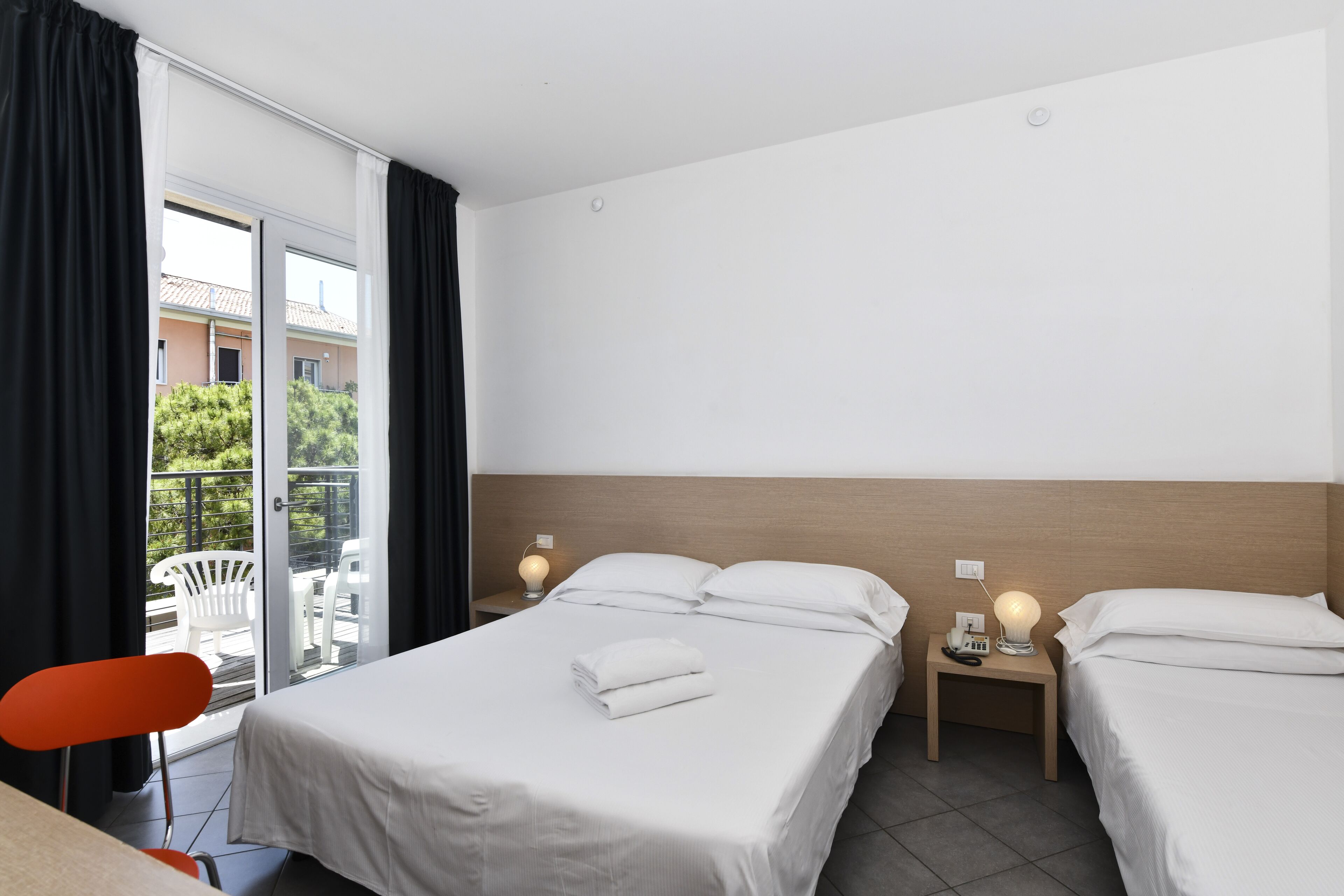 A hotel room with two beds, a balcony, and a view of the outside.