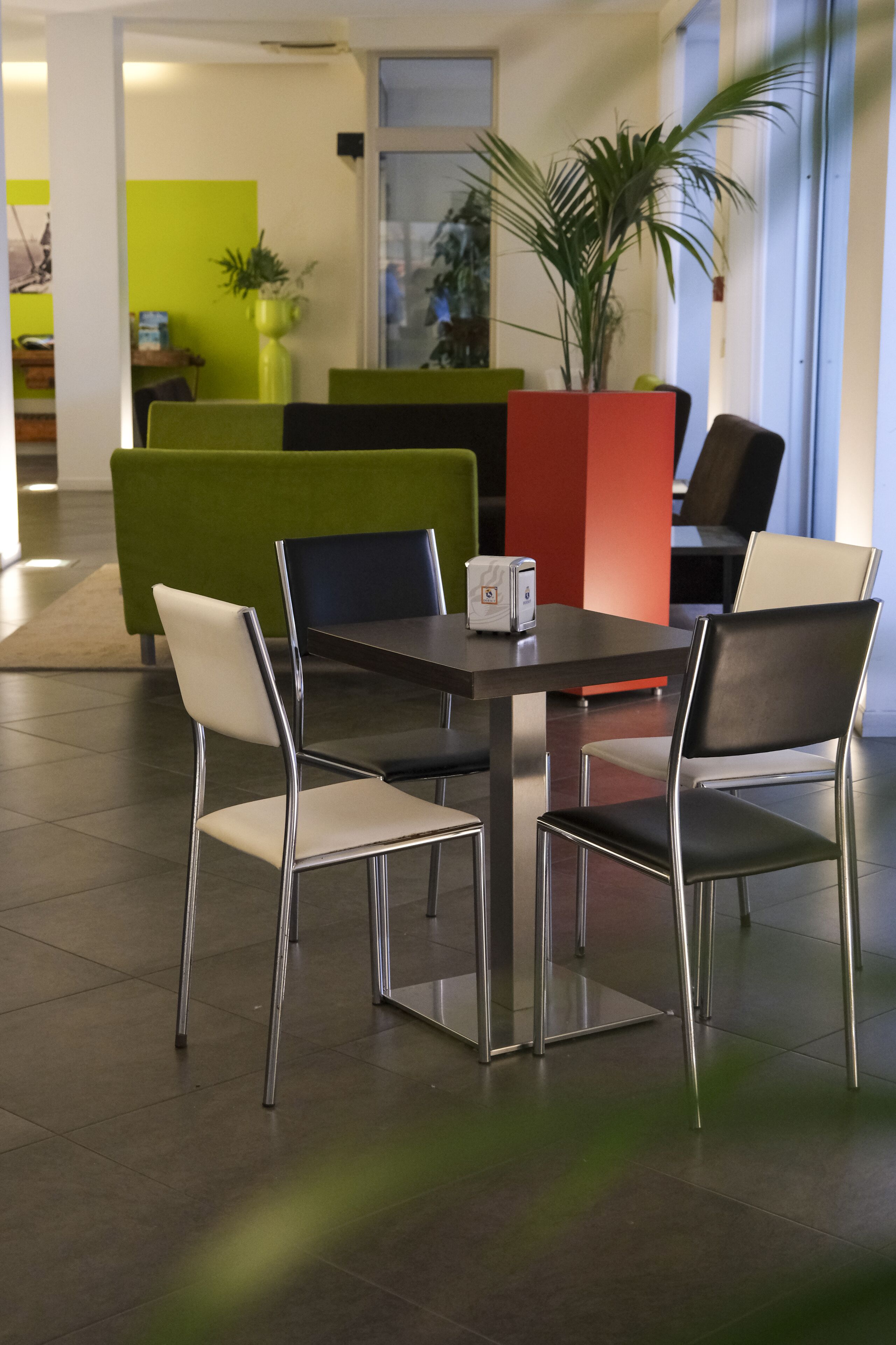 Un espace repas moderne comprenant une table et quatre chaises, une plante en pot et un paravent aux couleurs verte et rouge.