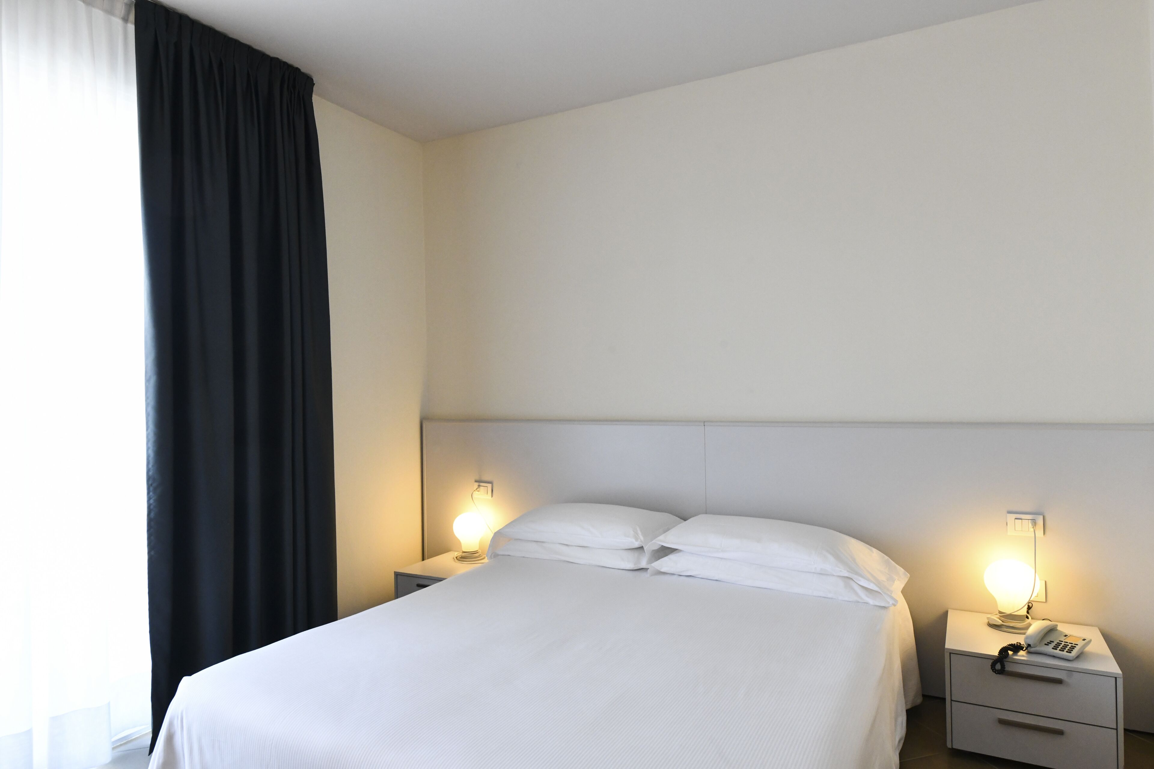 A hotel room with a bed, two bedside tables, a nightstand, and a lamp.