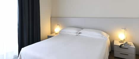 Una habitación de hotel con una cama, dos mesitas de noche y una lámpara.