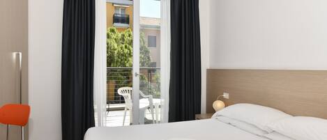 A hotel room with a bed, a chair, a table, and a view of a balcony with a railing.