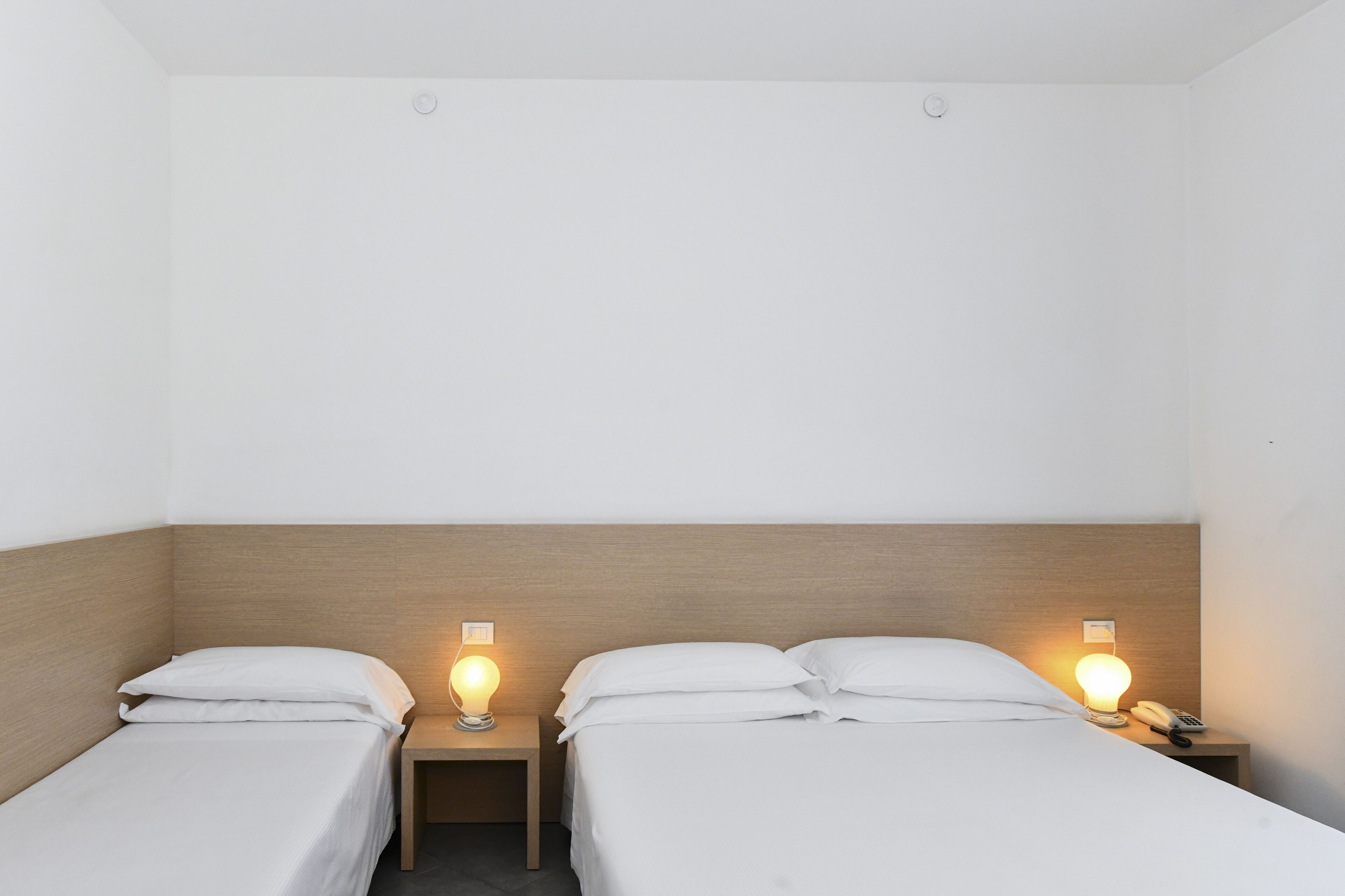 A room with two single beds, each with a nightstand and a bedside lamp.