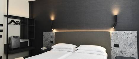 Una habitación de hotel moderna con una cama grande, una mesita de noche, un escritorio, un armario y una lámpara de pared.