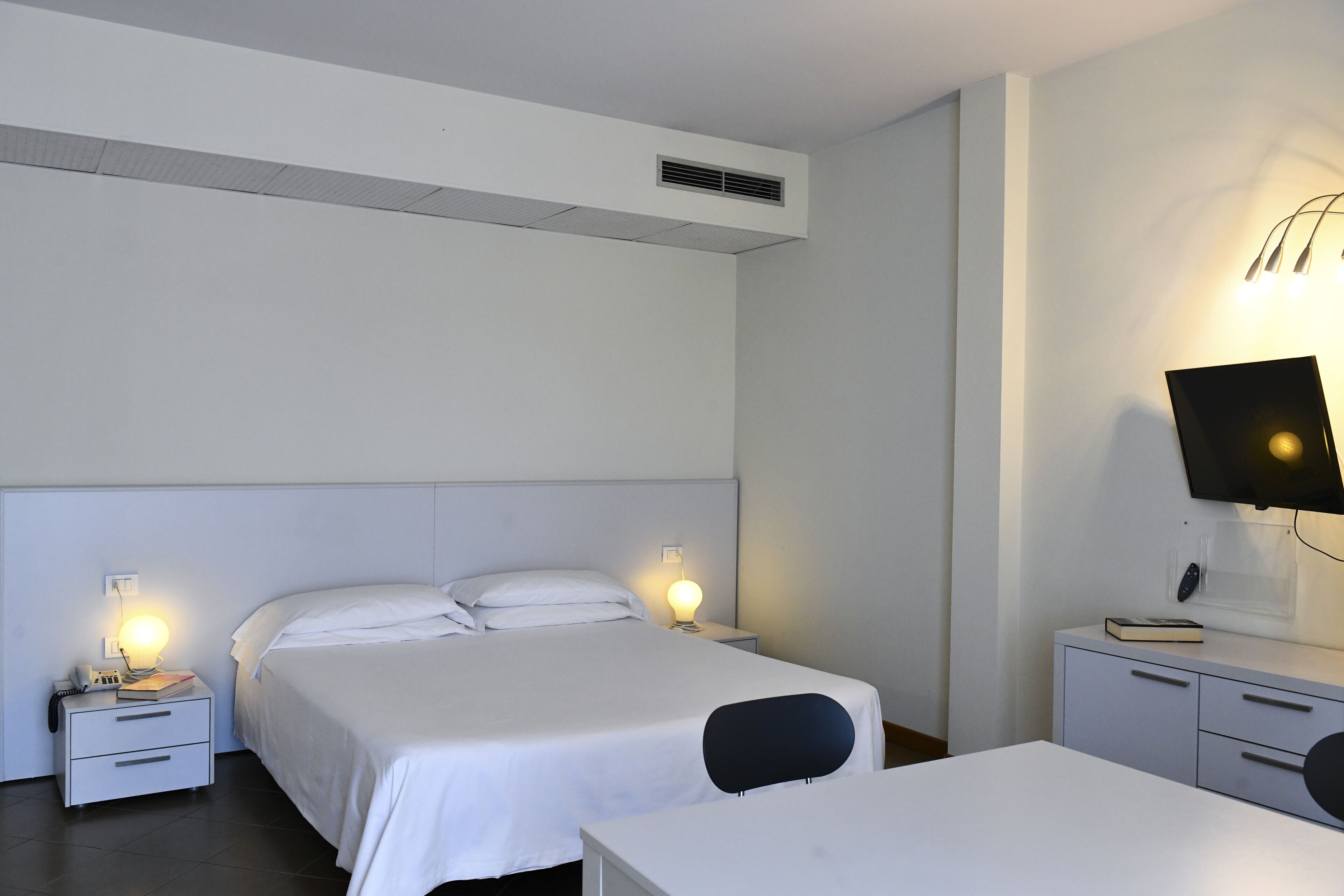 Habitació d'hotel amb un llit, taules de nit, escriptori i televisió.