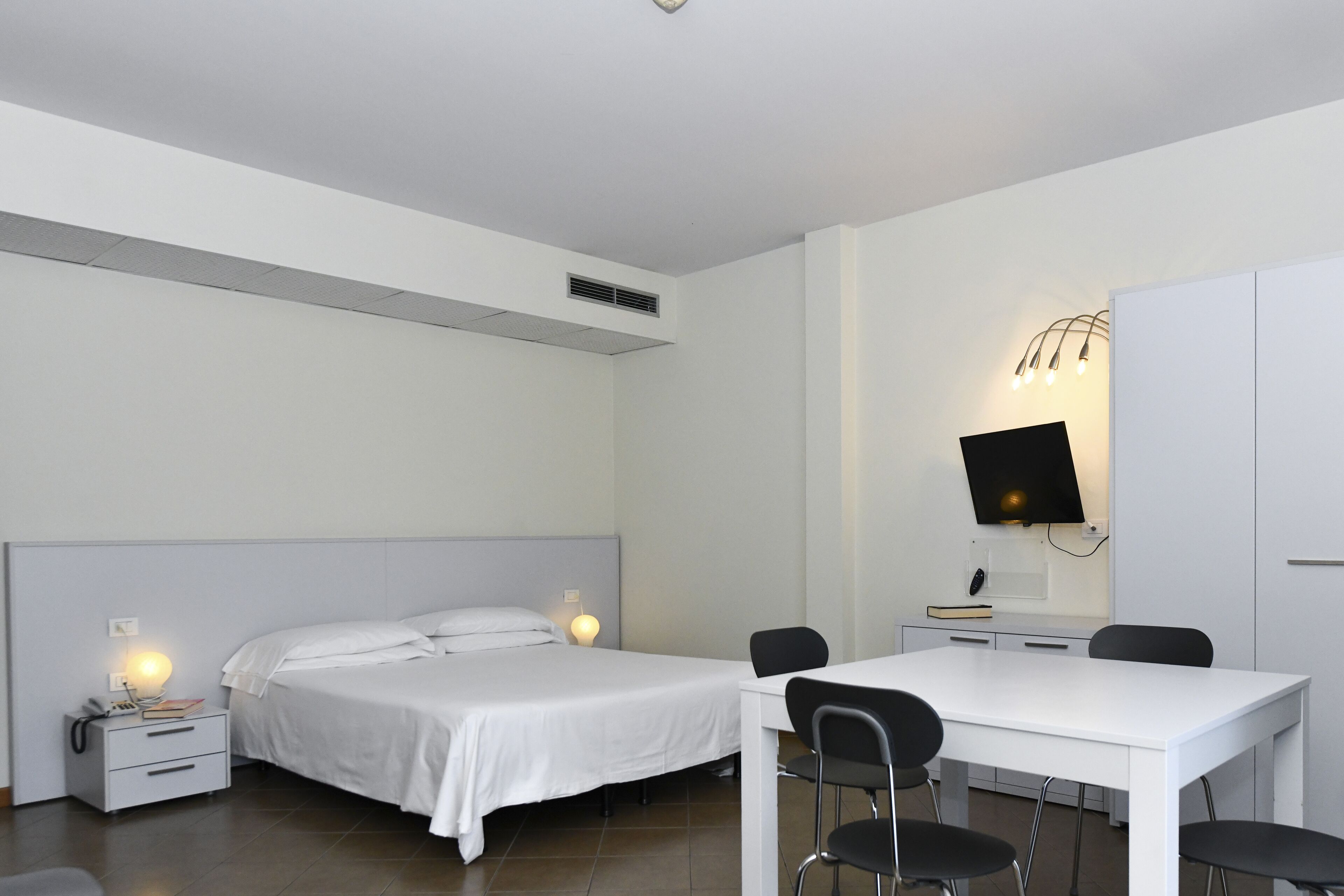 Ein Hotelzimmer mit zwei Einzelbetten, einem Schreibtisch mit Stühlen, einem flachbildfernseher an der Wand und einem weißen Kleiderschrank.