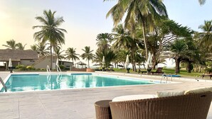 Una piscina con sillas de descanso y una silla de mimbre, rodeada de palmeras y un cielo despejado.