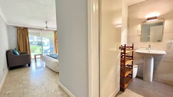 A hotel room with a sofa, a bed, a bathroom with a sink and mirror, and a view of the outside.