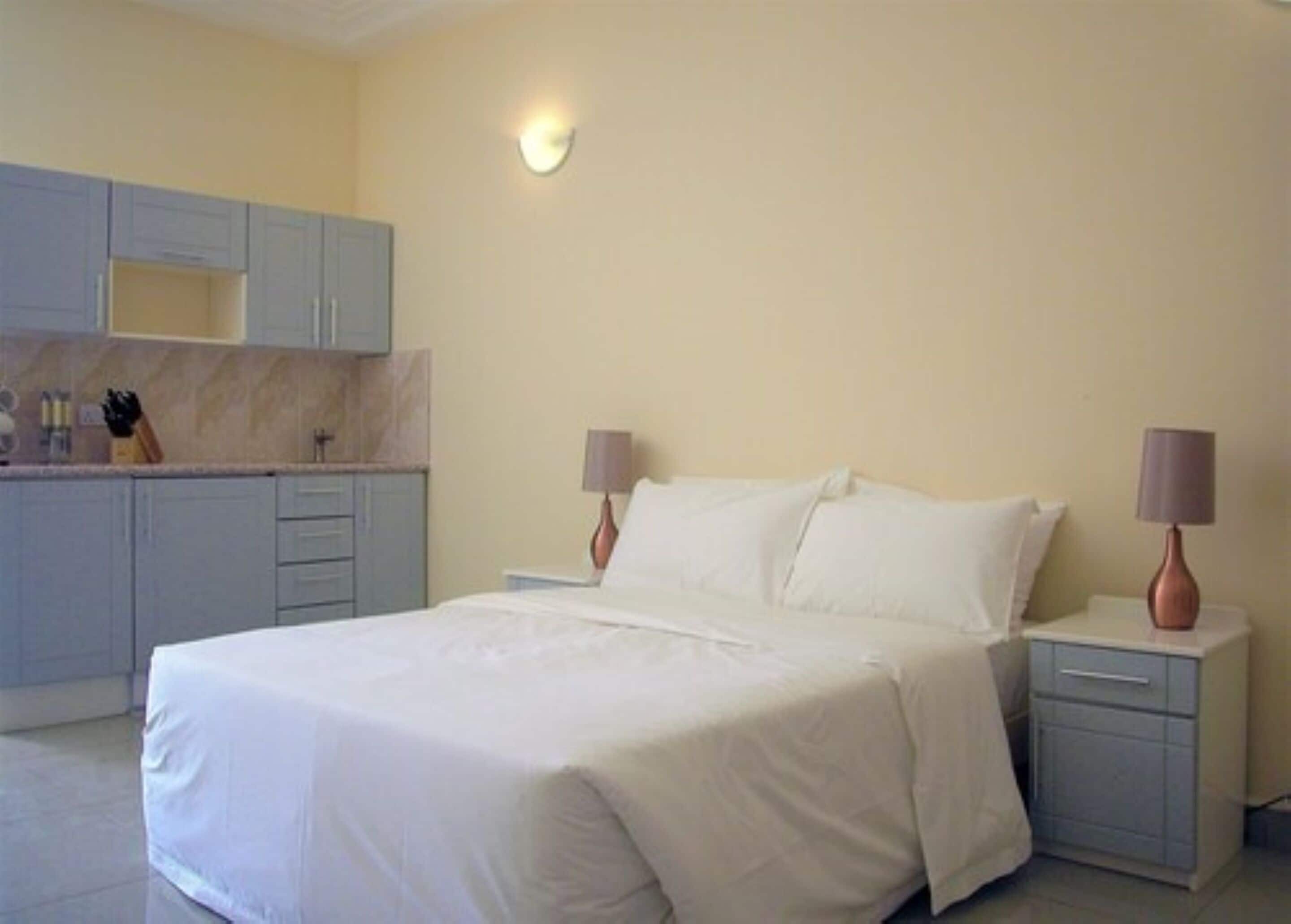 A bedroom with a bed, nightstands, and a small kitchenette.