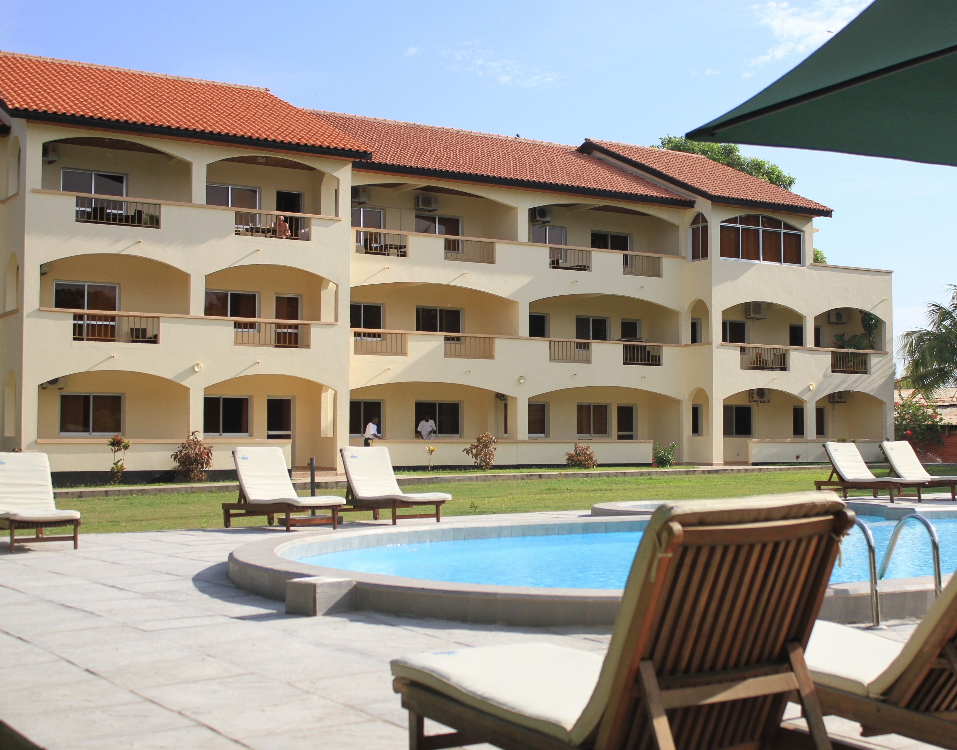 A multi-story hotel with a swimming pool, outdoor seating, and a red-tiled roof.