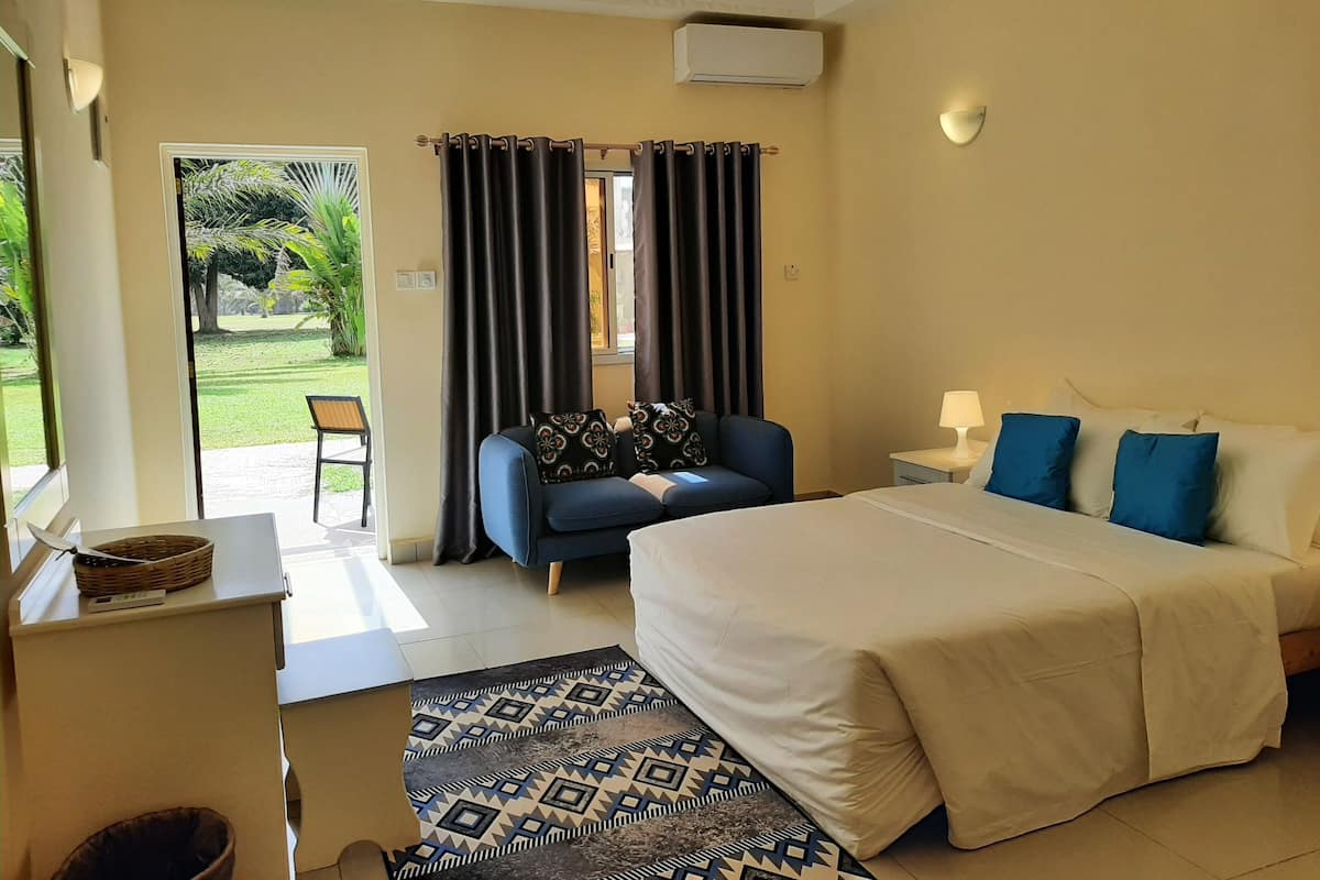 Ein Hotelzimmer mit Bett, Schreibtisch, Stuhl, einem Fenster mit Vorhängen und Blick auf einen Garten.