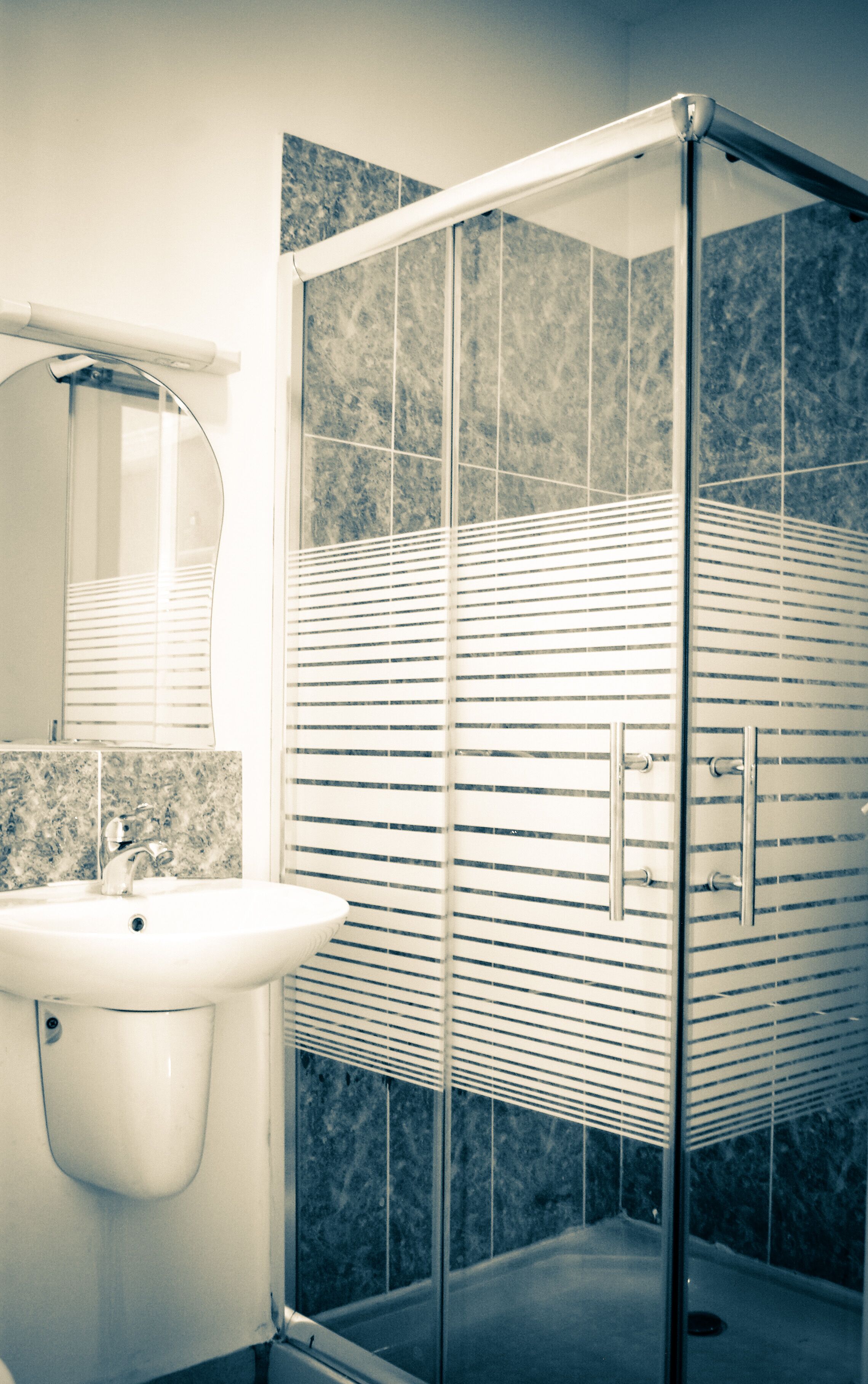 Un bagno con cabina doccia in vetro, lavandino bianco e piastrelle in marmo.