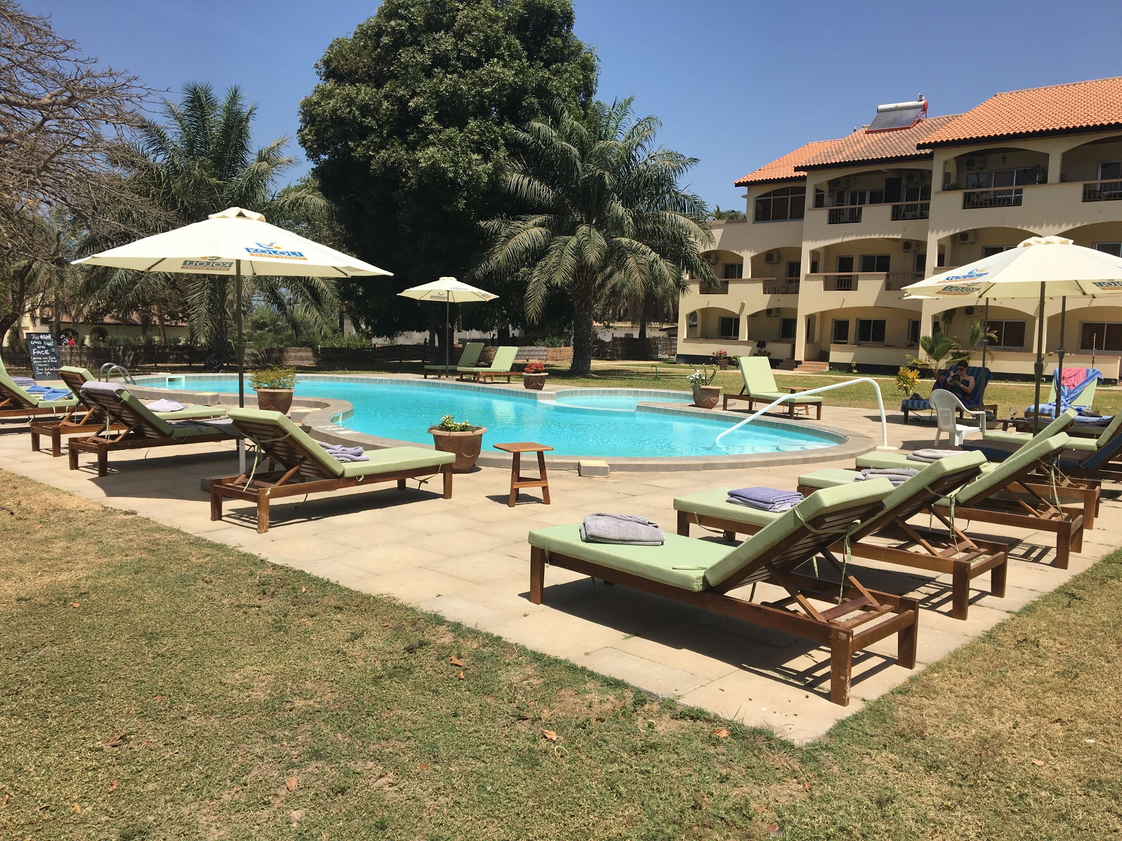 A pool area with lounge chairs and umbrellas, surrounded by a building with a tiled roof.