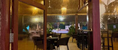 An indoor dining area with tables and chairs, a ceiling with a woven pattern, and hanging lights.