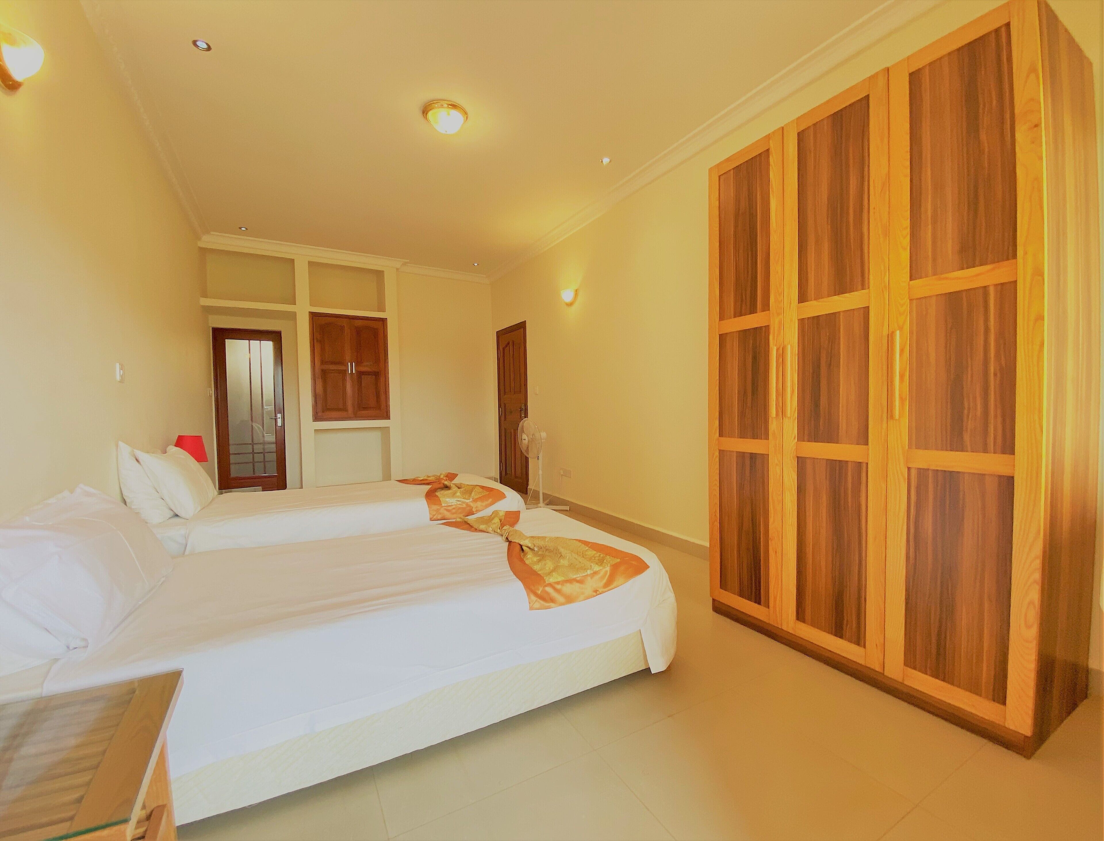 Een hotelkamer met twee bedden, een grote houten garderobe en een plafondventilator.