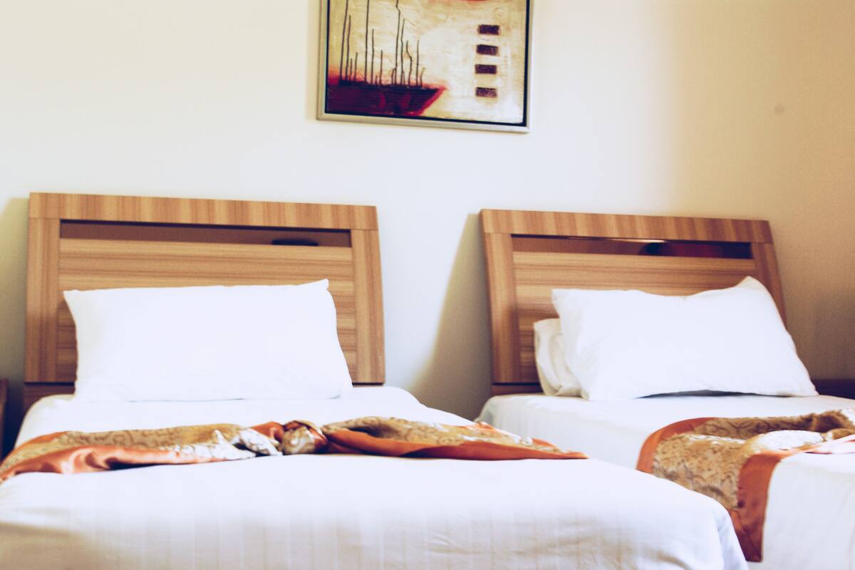 Ein Hotelzimmer mit zwei Betten, jeweils mit hölzernen Kopfteilen und weißer Bettwäsche.