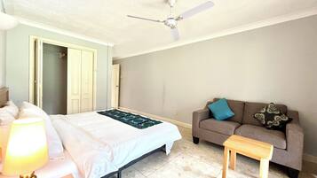 Quarto com cama, ventoinha no teto, sofá, mesinha e abajur.