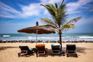 Una playa con tres sillas de madera, una sombrilla de paja y una palmera.