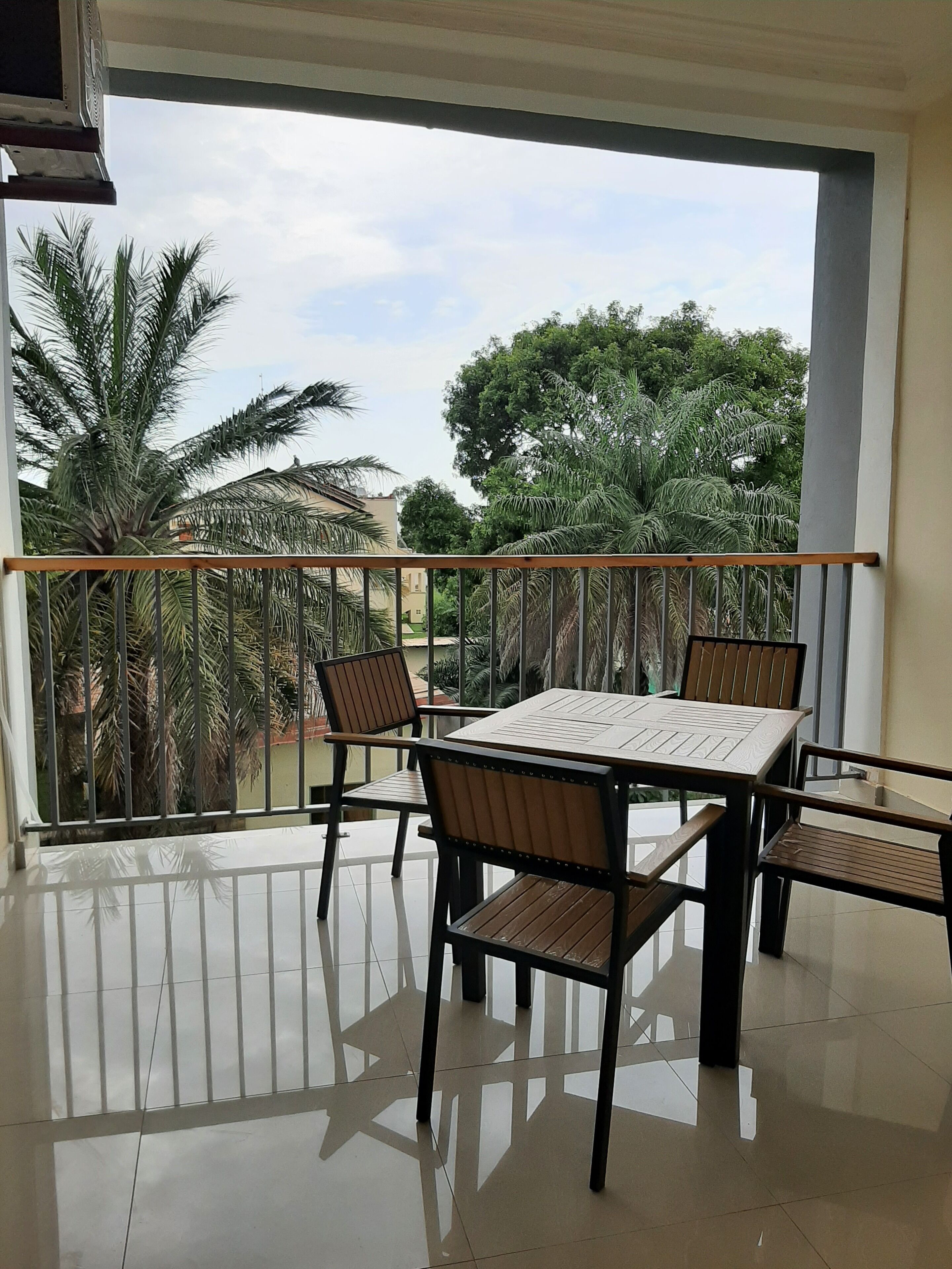 Een balkon met een tafel en stoelen, een hekwerk en uitzicht op palmbomen en gebouwen.