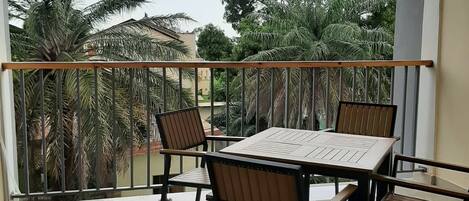 A balcony with a table and chairs, a railing, and views of palm trees and buildings.