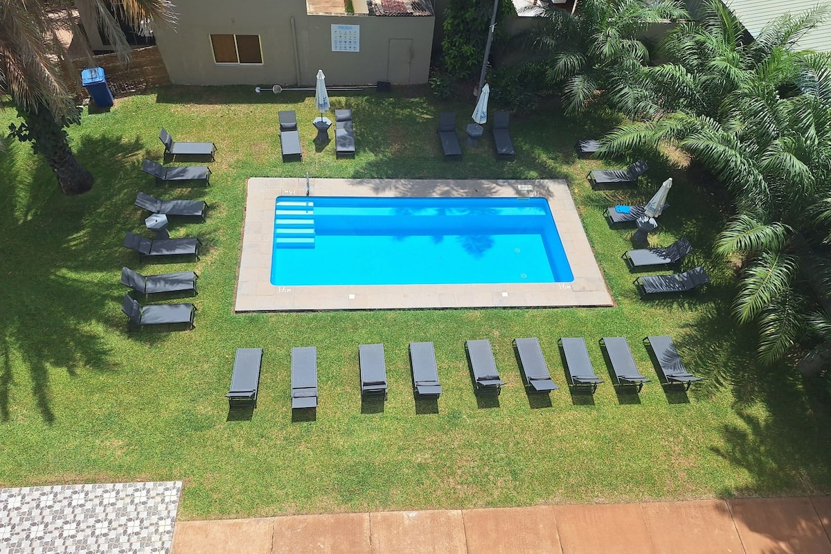 Ein rechteckiger Swimmingpool, umgeben von Liegestühlen und einer kleinen Gartenanlage mit Palmen.