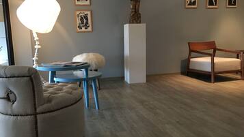 A modern living room with a round blue table, a beige armchair, a wooden chair, and a white pedestal with a statue.
