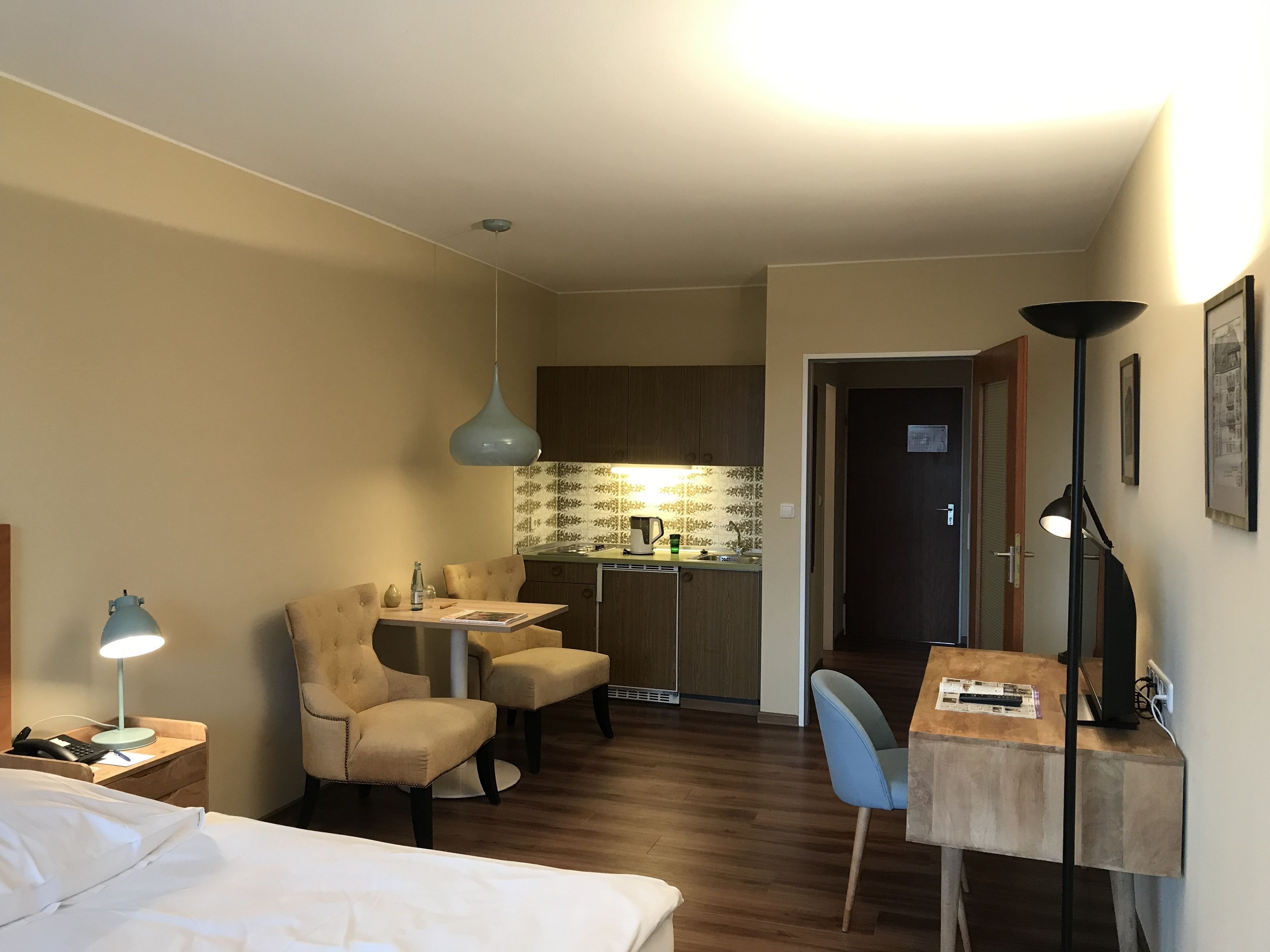 Una habitación de hotel pequeña con cama, escritorio, silla, kitchenette y zona de comedor.