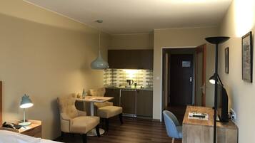 Una habitación de hotel pequeña con cama, escritorio, silla, kitchenette y zona de comedor.
