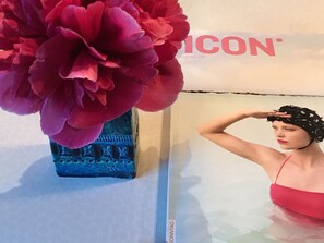 Una persona con traje de baño rojo de pie frente a una exhibición con una flor roja grande y un jarrón azul.