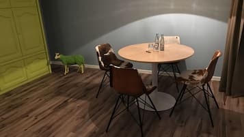 Um quarto com uma mesa redonda de madeira, quatro cadeiras, uma porta verde e uma pequena decoração de ovelha verde.