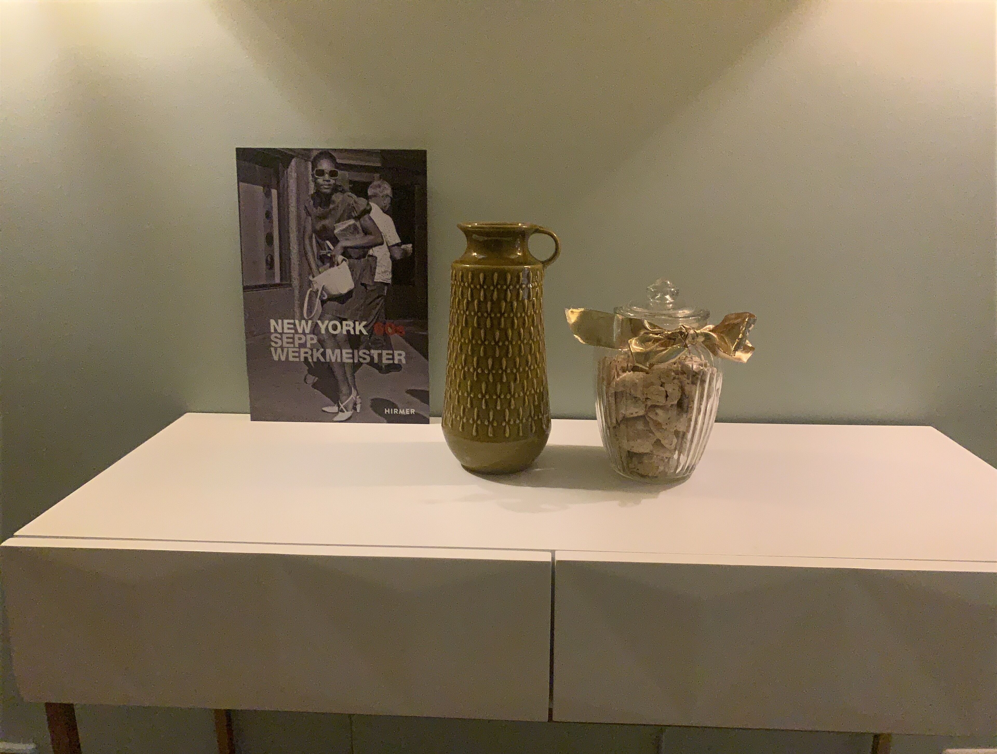 Une table blanche avec une affiche, un vase à texture et un bocal en verre décoré d’un ruban.
