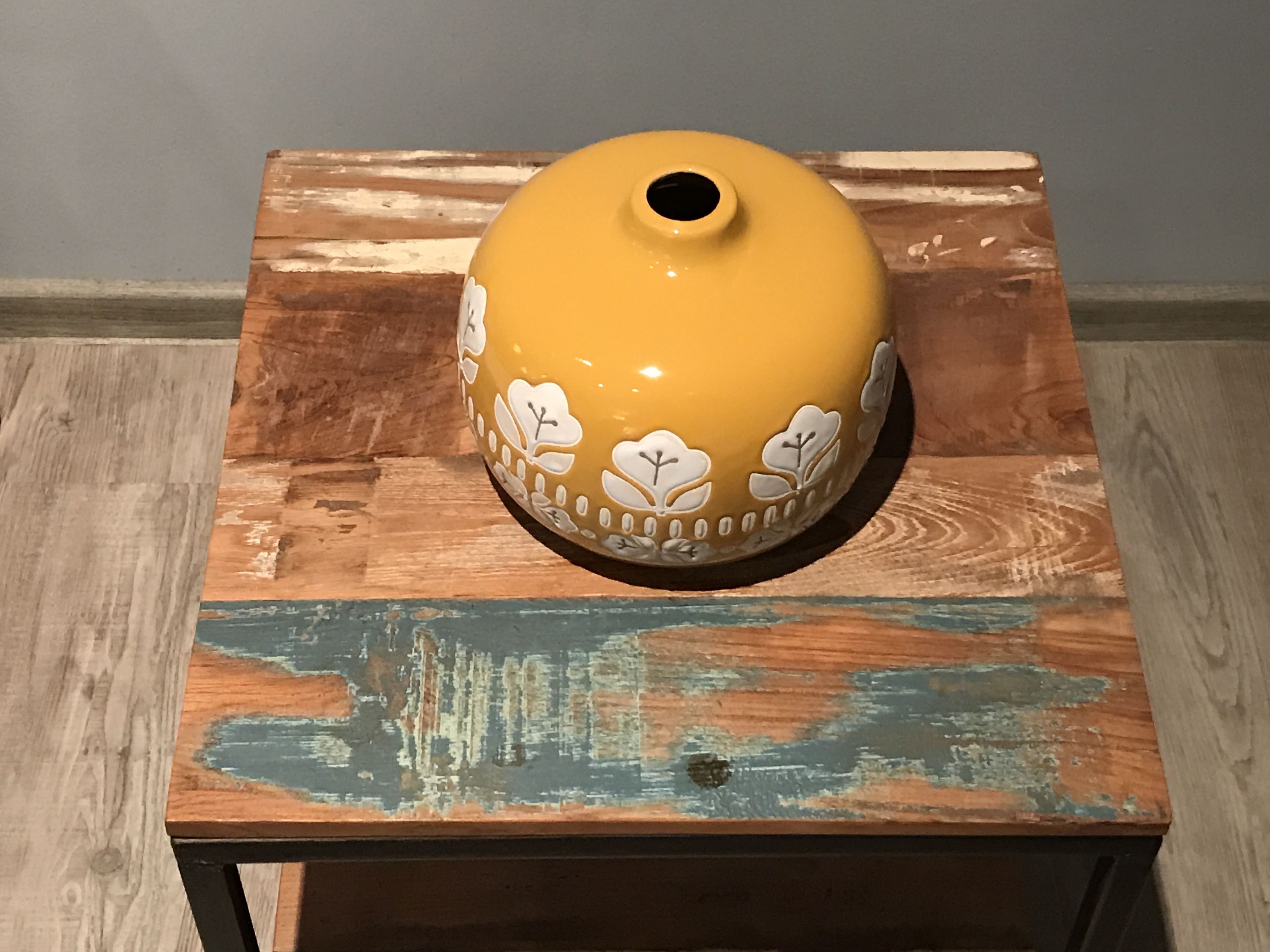 A yellow ceramic pot with floral designs on a wooden table with a distressed blue paint finish.