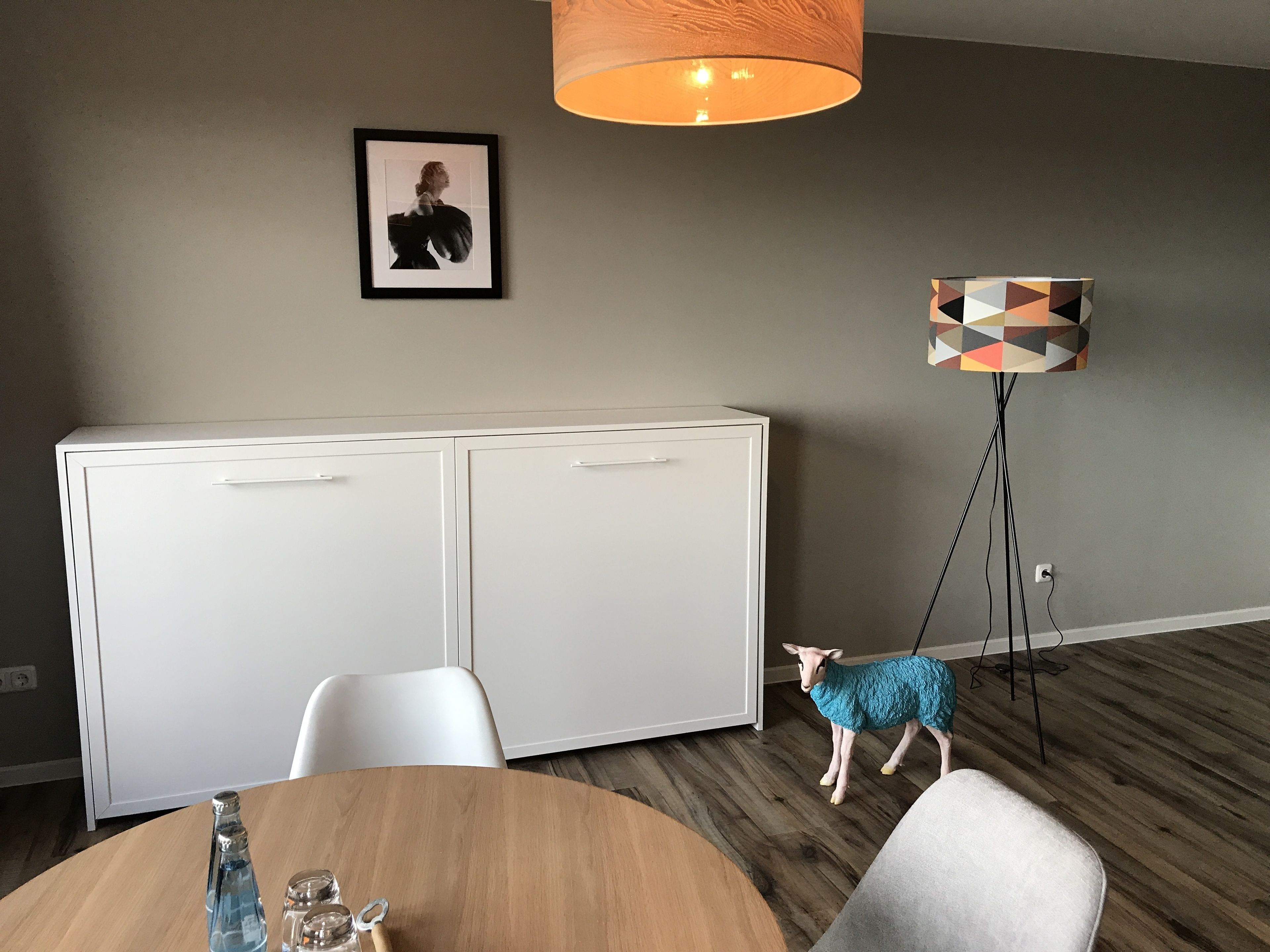 Une pièce moderne avec un meuble blanc, une table ronde en bois, une petite figurine et un lampadaire au design géométrique.