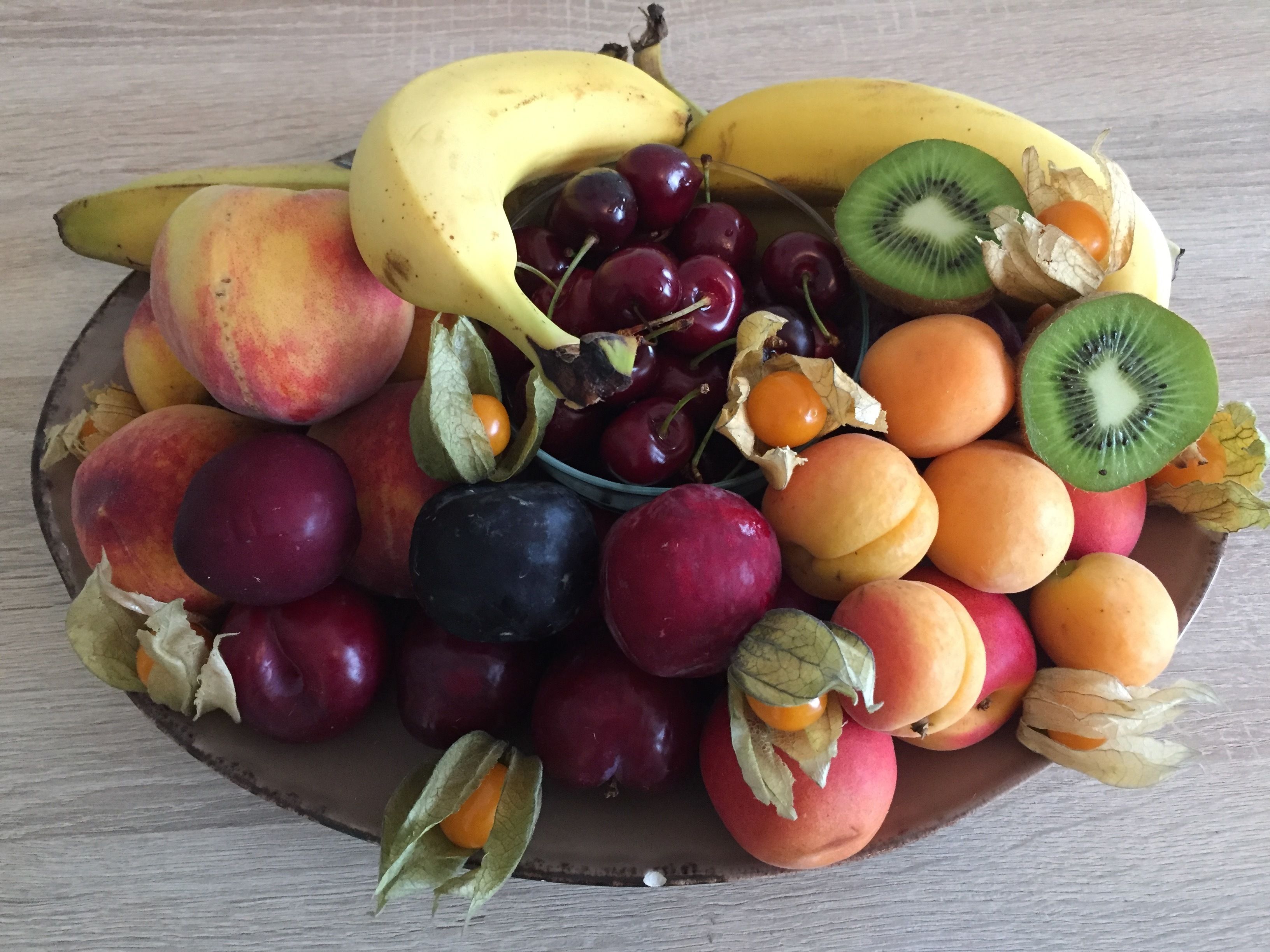A wooden table with a variety of fruits including bananas, cherries, peaches, plums, apricots, and kiwi.