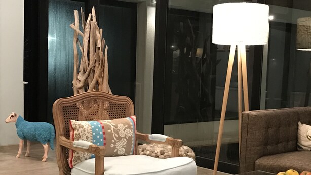 A modern living room with a glass coffee table, a wooden chair with a cushion, a sofa, and a lamp. - Das Hotel Ostseeblick (Luetjenburg)