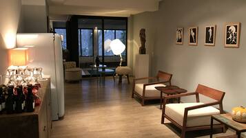 Una sala moderna con suelo de madera, un sofá, una mesa de centro y una mesa de comedor. Hay cuadros en la pared y una lámpara sobre la mesa.