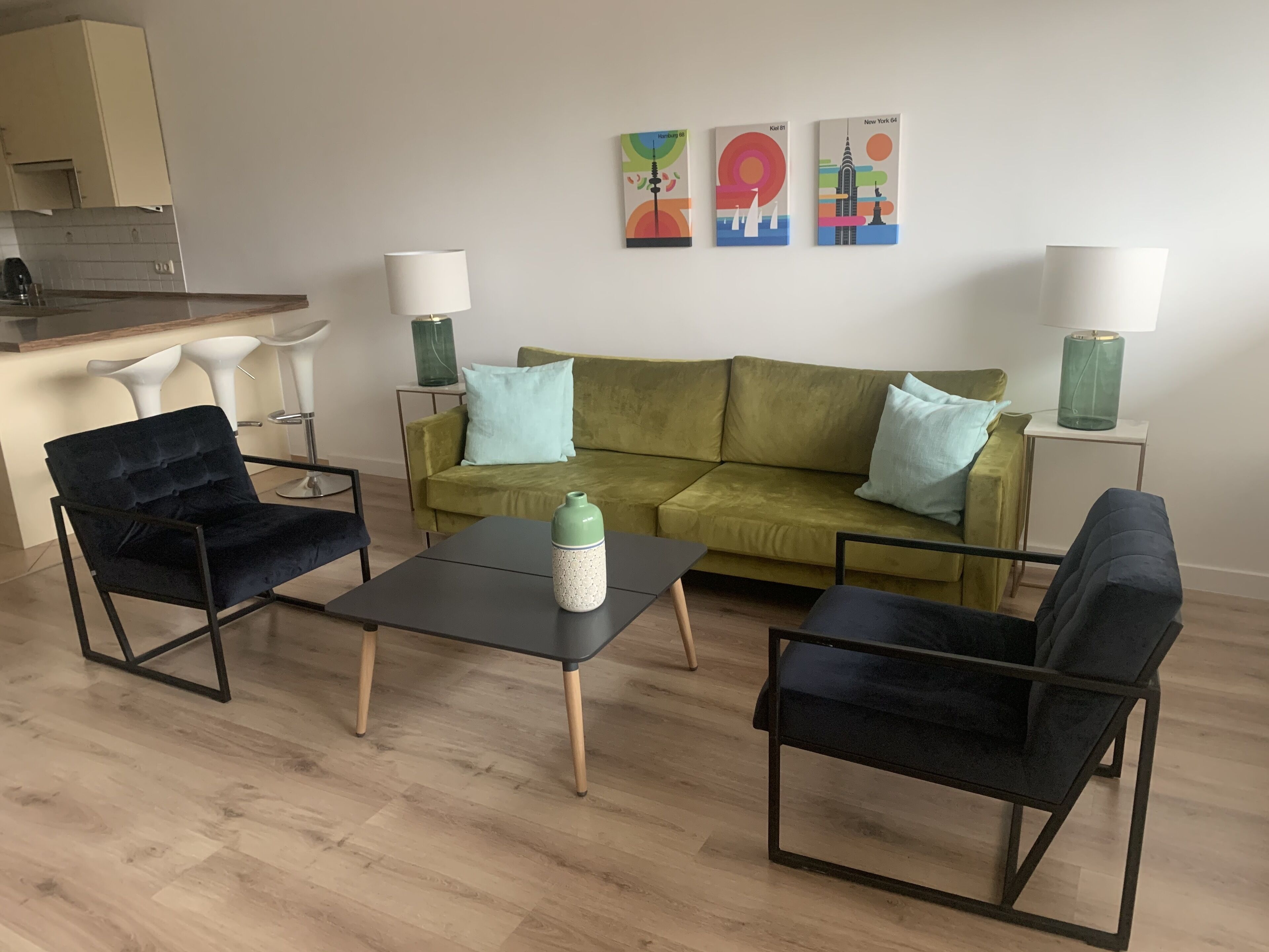 A living room with a green sofa, two black armchairs, a coffee table, and three wall-mounted lamps.