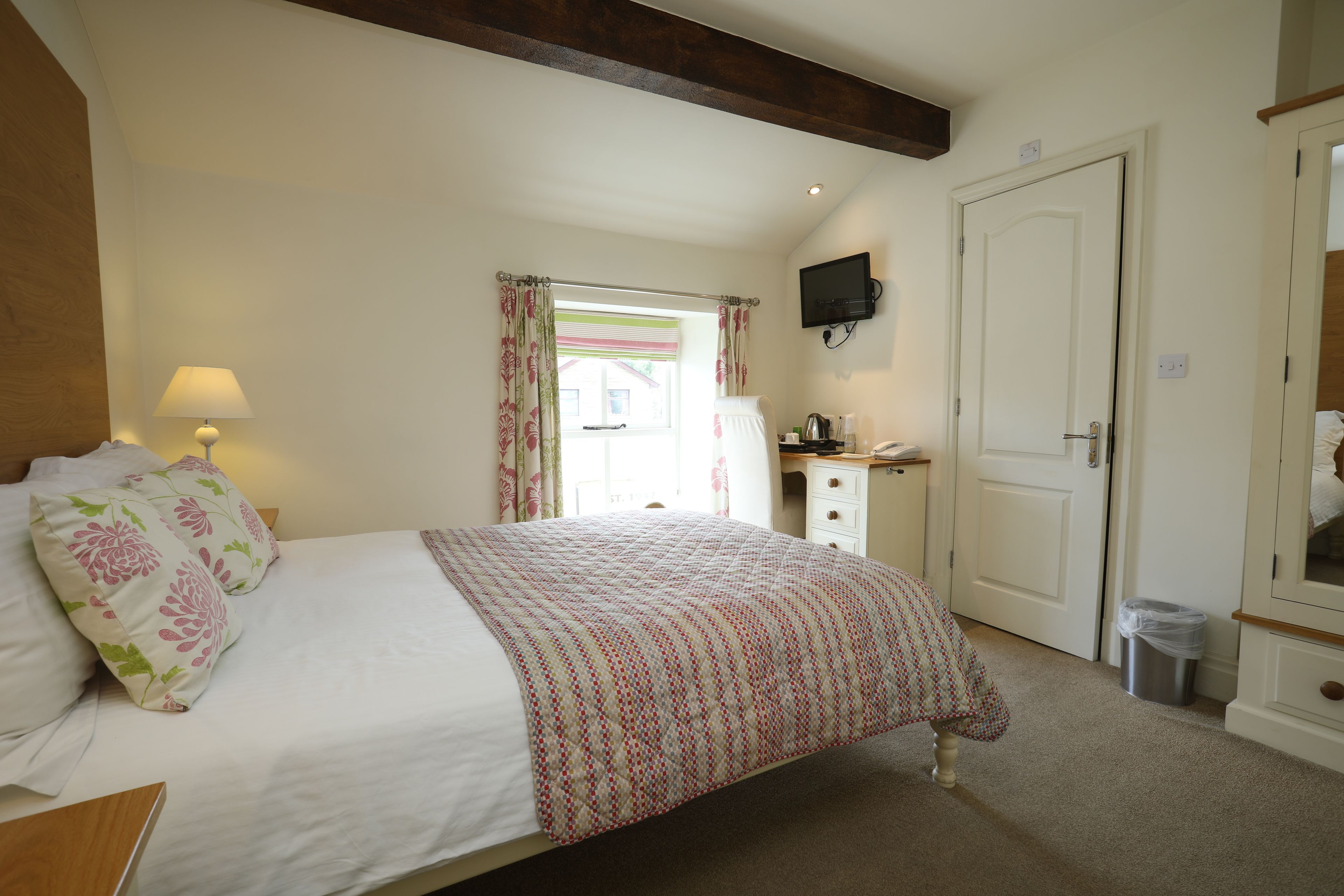 A bedroom with a bed, a bedside lamp, a dresser, a television, and a door.