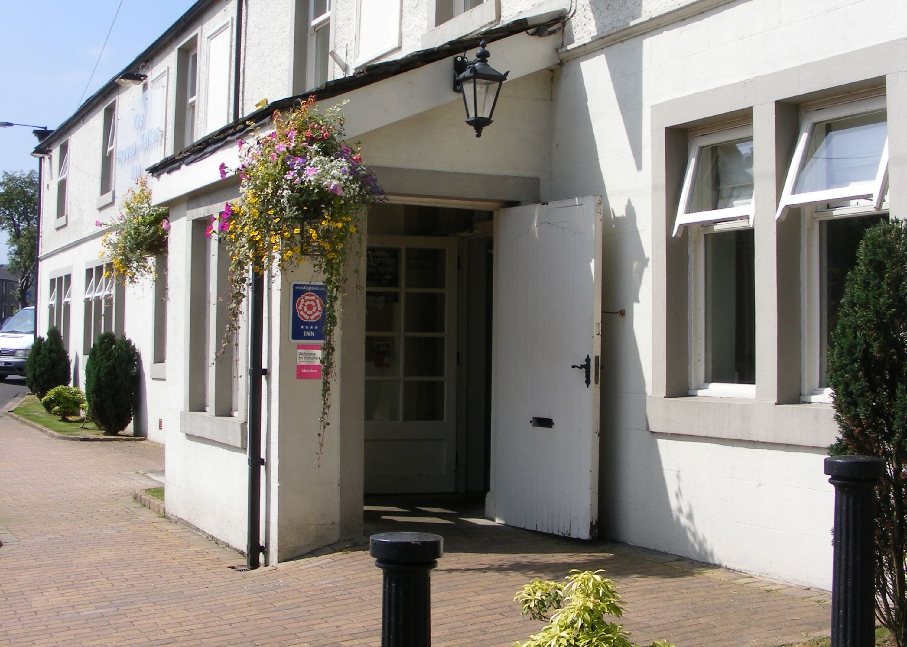 A traditional building with a white facade, a door with a glass panel, and hanging flower baskets.